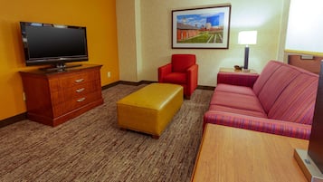 Une chambre d’hôtel équipée d’un téléviseur à écran plat, d’un fauteuil rouge, d’un pouf jaune, d’un canapé à rayures et d’un tableau encadré accroché au mur.