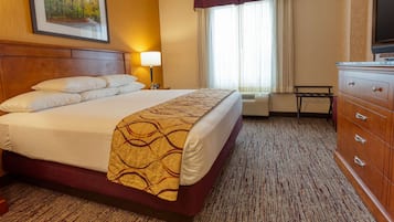 A hotel room with a large bed, a wooden headboard, a desk with a chair, a television, and a window with curtains.