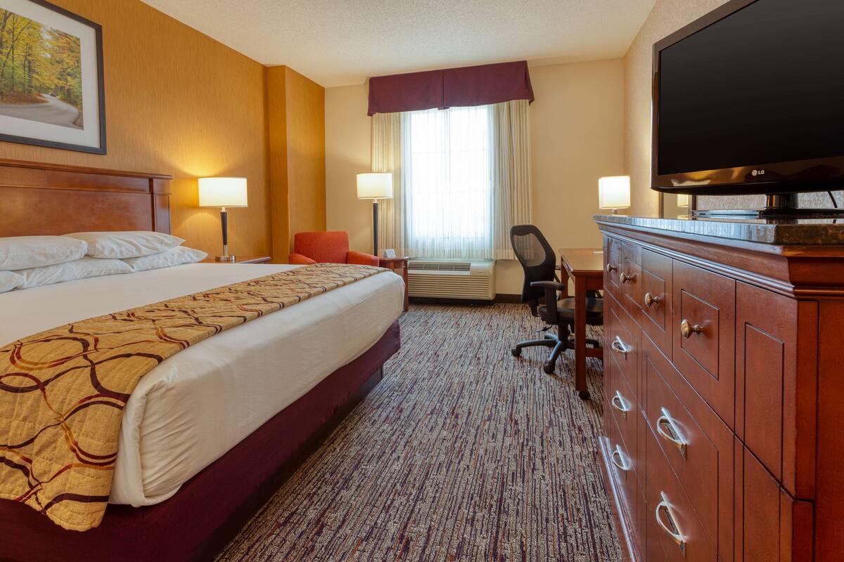 Ein Hotelzimmer mit einem großen Bett, einem Schreibtisch mit Stuhl, einem Fernseher und einem Schminktisch.