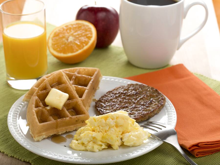 Une assiette avec des gaufres, des œufs brouillés et une galette, accompagnée d’un verre de jus d’orange et d’une tasse de café.