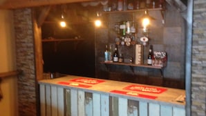 Una zona de bar con un mostrador de madera rústica, paredes de piedra y una variedad de botellas y vasos.