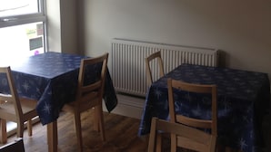 Un comedor con cuatro mesas, cada una cubierta con mantel azul decorado con motivos náuticos. En la pared, sobre las mesas, hay cuatro espejos redondos.