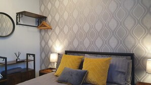 Un dormitorio ordenado con una cama, dos mesitas de noche, una lámpara colgante y un espejo montado en la pared.
