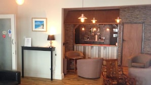 Una habitación acogedora con suelo de madera, una zona de bar con un espejo y un espacio de descanso con un sofá y sillas de madera.