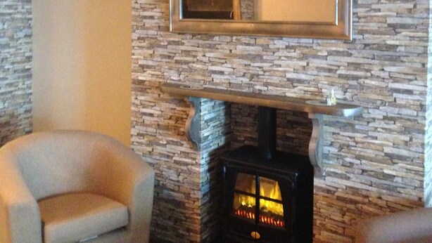 Una sala de estar con chimenea de piedra, un espejo grande y dos sillones.