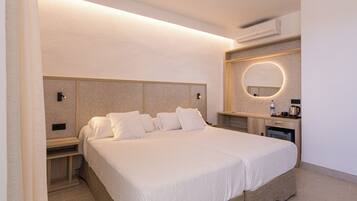 Camera d'hotel con un letto grande, comodini, una scrivania integrata, uno specchio rotondo e un condizionatore d'aria a parete.