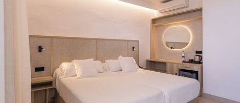 A hotel room with a large bed, bedside tables, a built-in desk, a round mirror, and a wall-mounted air conditioner.