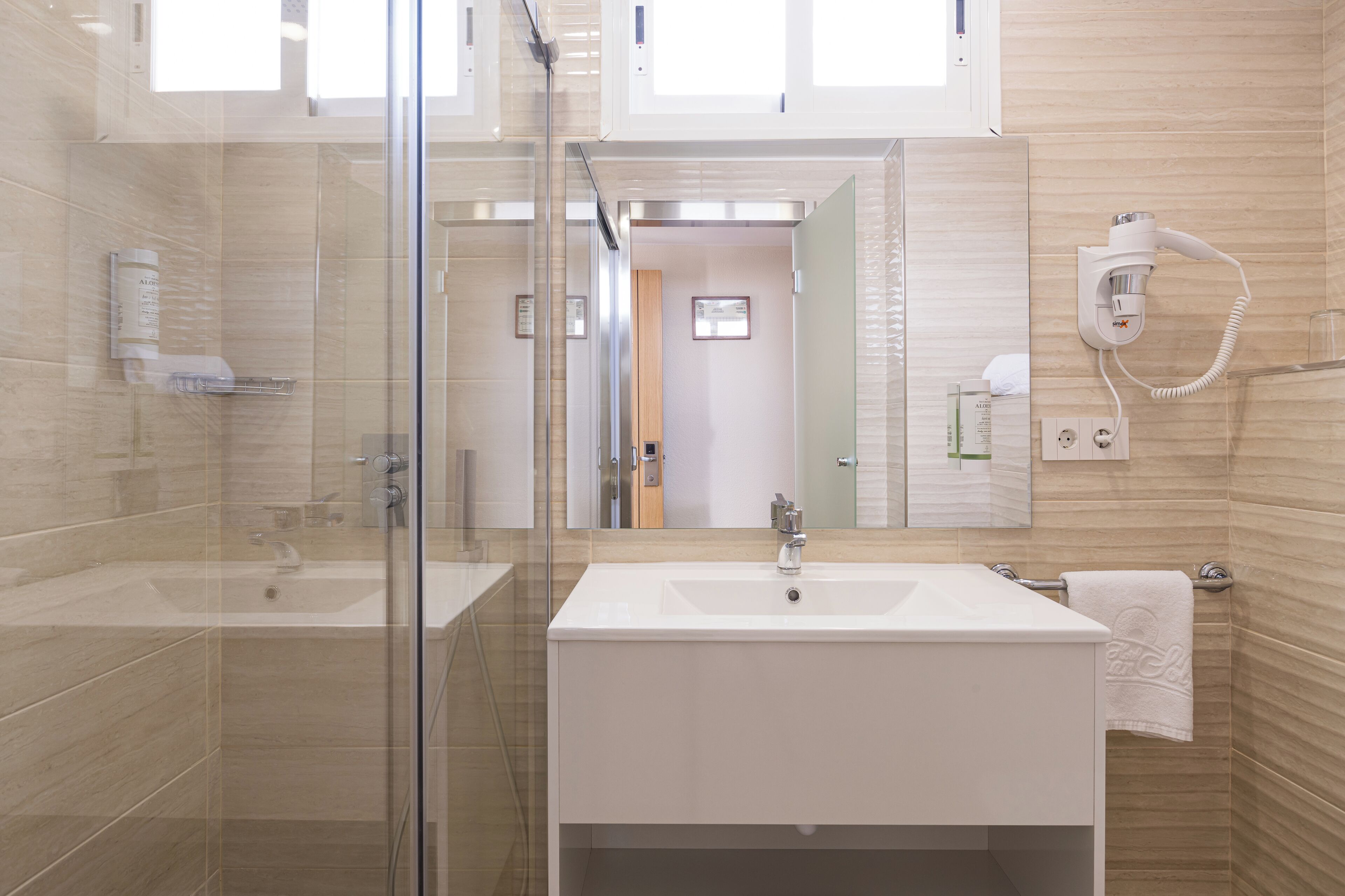 A modern bathroom with a glass shower enclosure, a white sink, and a hairdryer mounted on the wall.