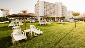 A hotel courtyard with white lounge chairs and thatched umbrellas, surrounded by modern buildings. - Hotel Gran Sol Ibiza (Sant Antoni de Portmany)