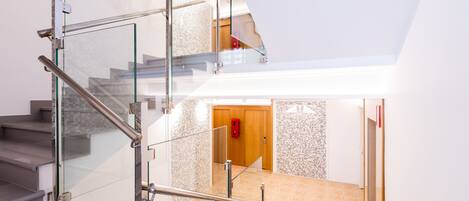 Un interior moderno con una escalera de cristal, una puerta de madera y un suelo de baldosas.