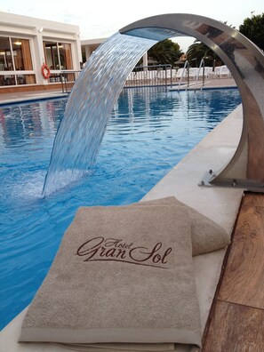 Une piscine agrémentée d’une cascade, d’une bouée de sauvetage et d’une serviette portant l’inscription « Hôtel Gran Sol ».