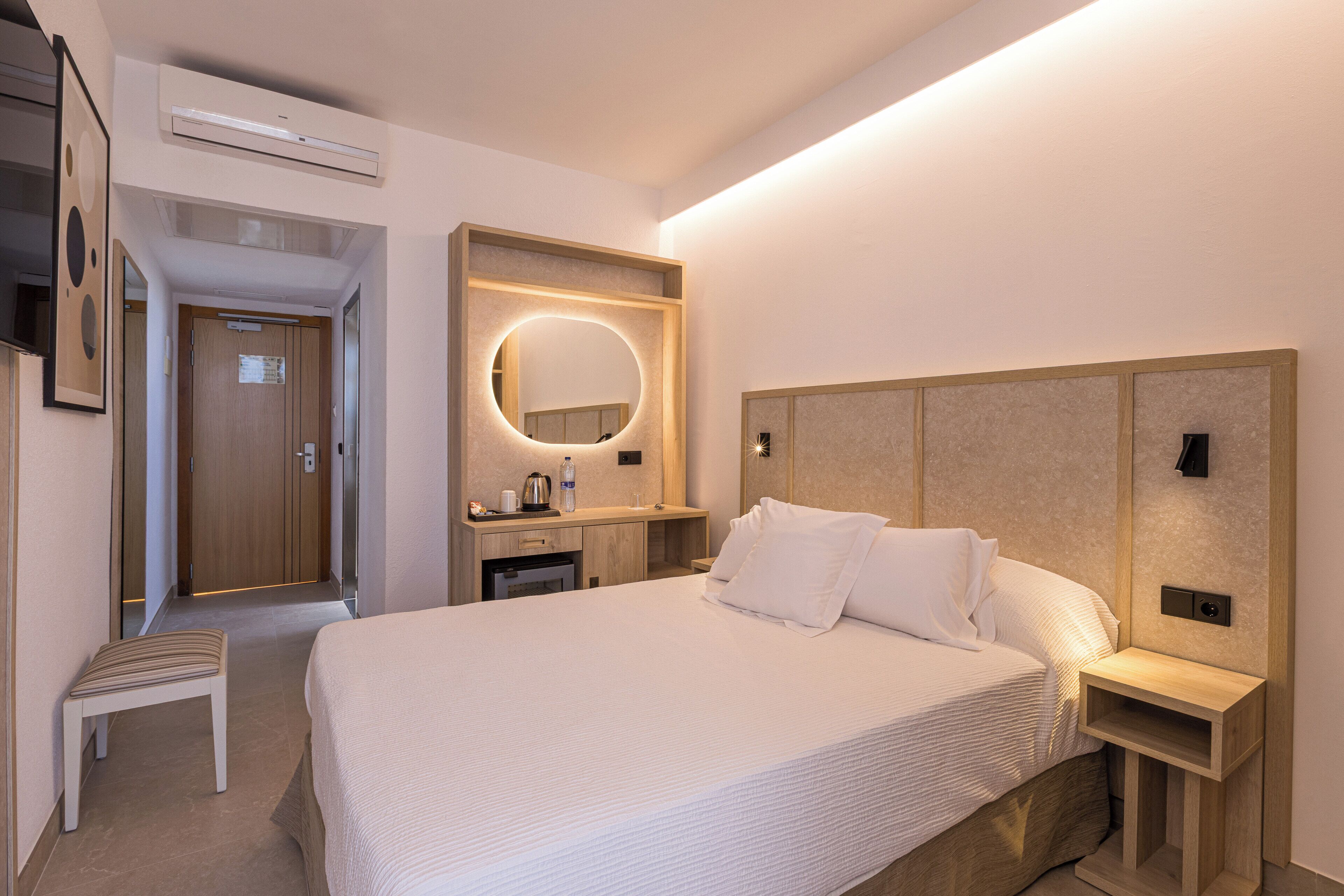 A hotel room with a large bed, a bedside table, a mirror, a small desk, and a chair.