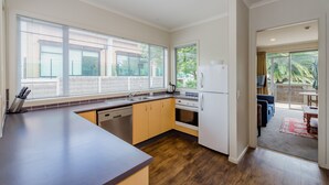 A modern kitchen with large windows, a dishwasher, oven, and a refrigerator. - Raumati Sands Resort (Paraparaumu)