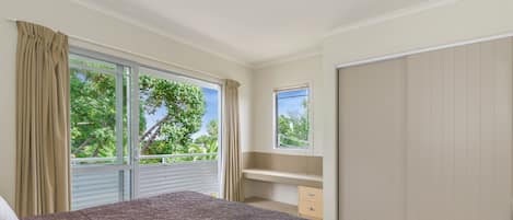 A bedroom with a large bed, a dresser, a mirror, and a sliding door to a balcony.