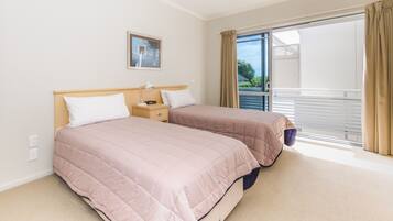 A hotel room with two beds, a bedside table with a lamp, a window with curtains, and a view of the outside.