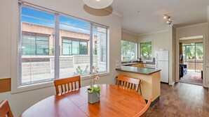 A modern kitchen with a central island, large windows, and a dining area with a wooden table and chairs. - Raumati Sands Resort (Paraparaumu)