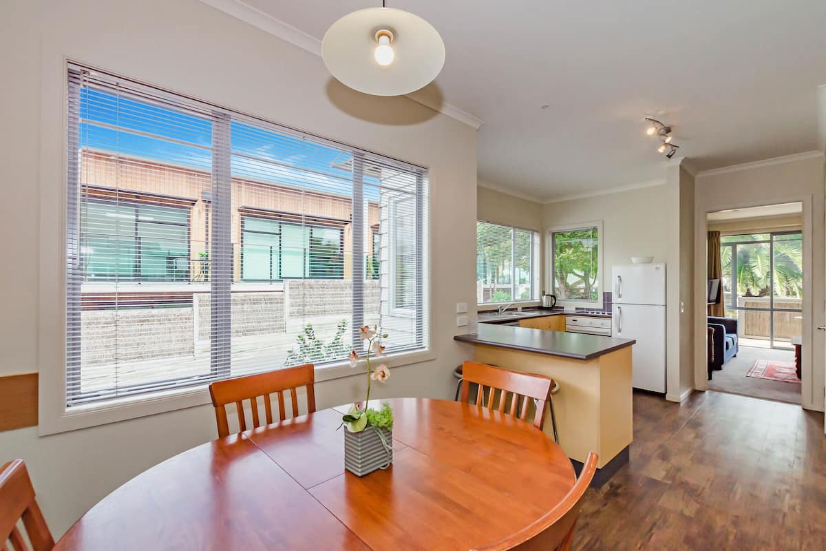 Una cocina moderna con una isla central, ventanas amplias y un comedor con mesa y sillas de madera.