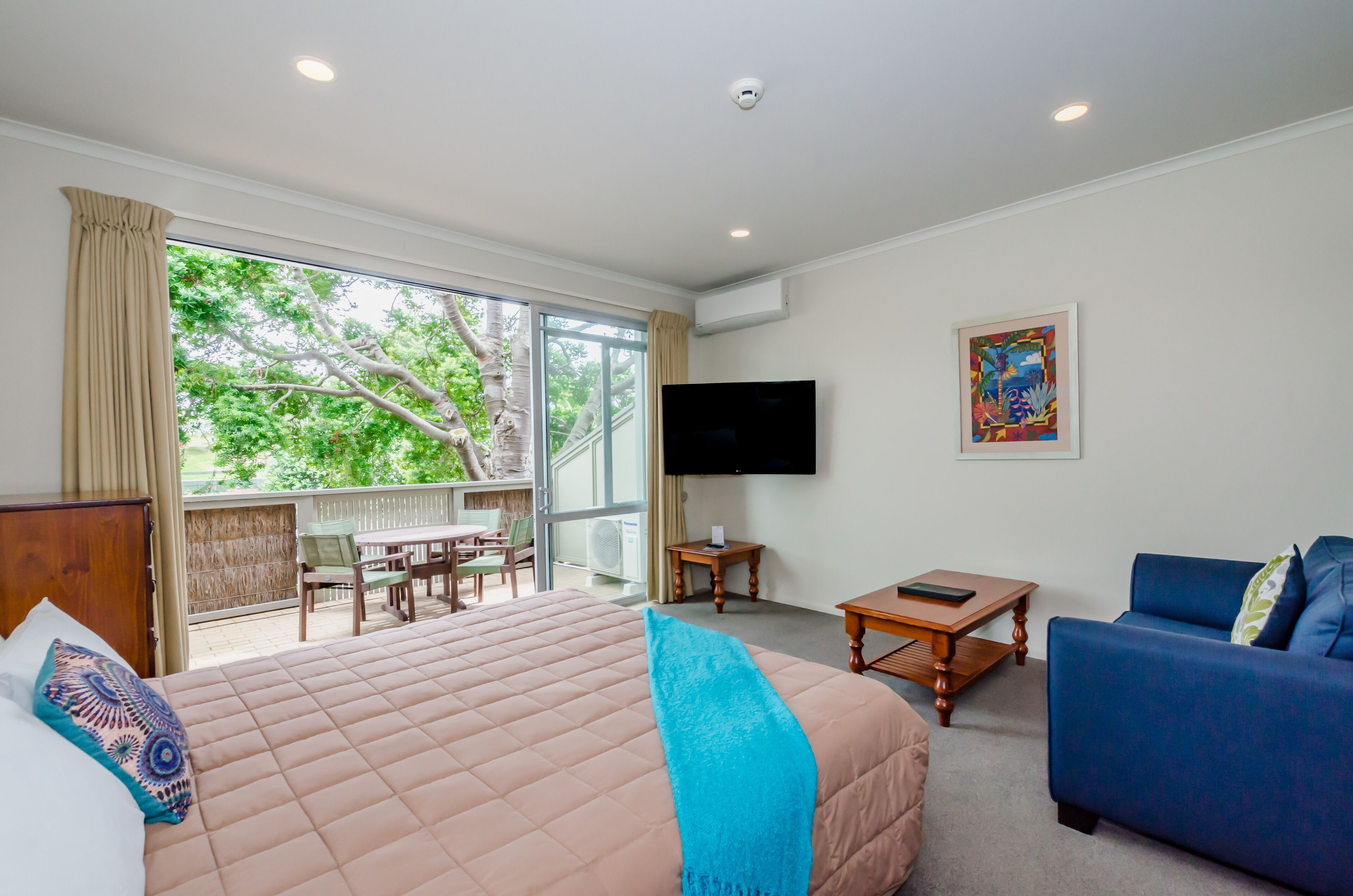 A hotel room with a large bed, a blue sofa, a TV, and a balcony with a table and chairs.