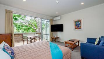 A hotel room with a large bed, a blue sofa, a TV, and a balcony with a table and chairs.
