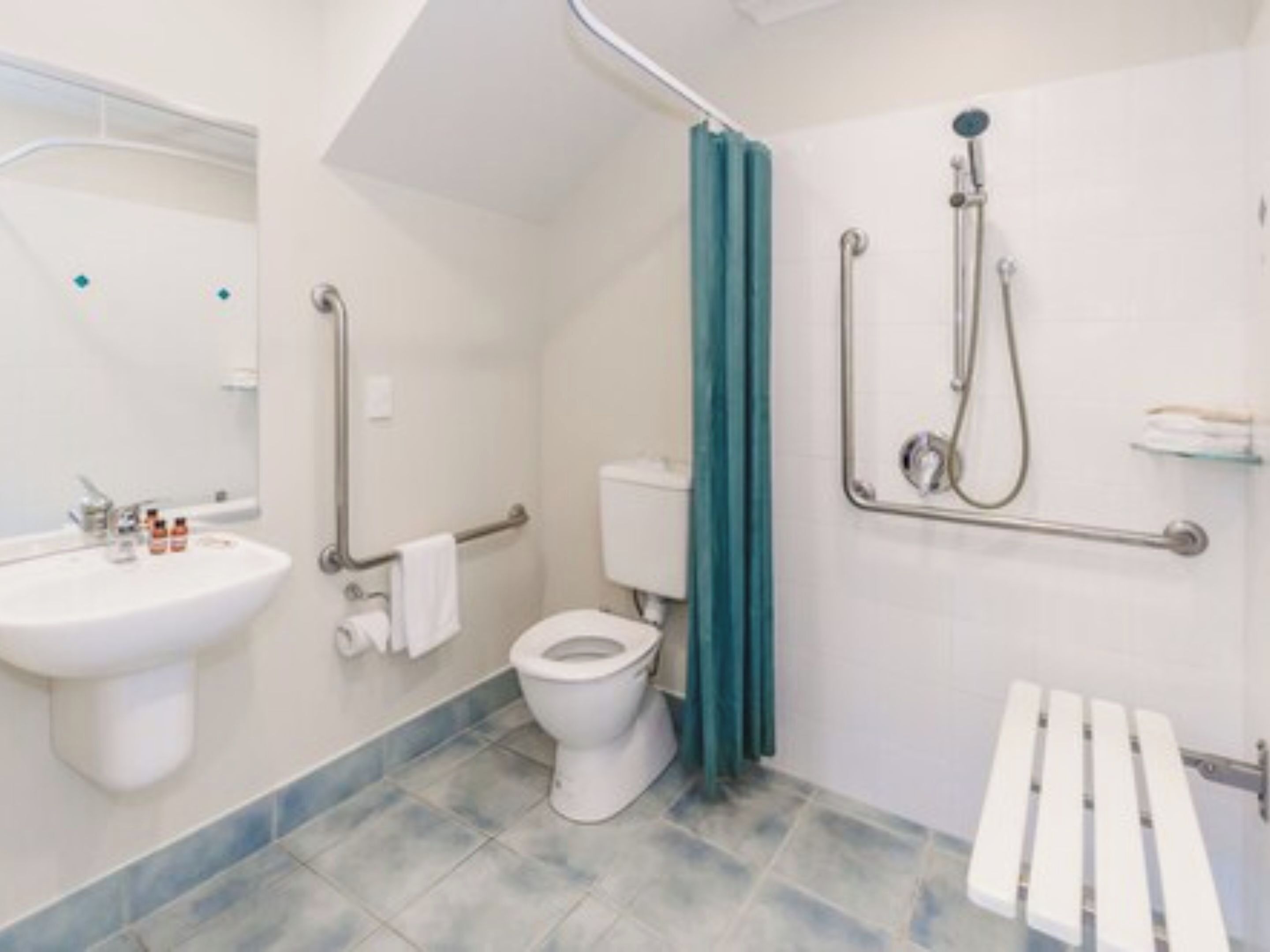 A bathroom with a white sink, toilet, and shower. There are grab bars next to the toilet and a shower curtain.