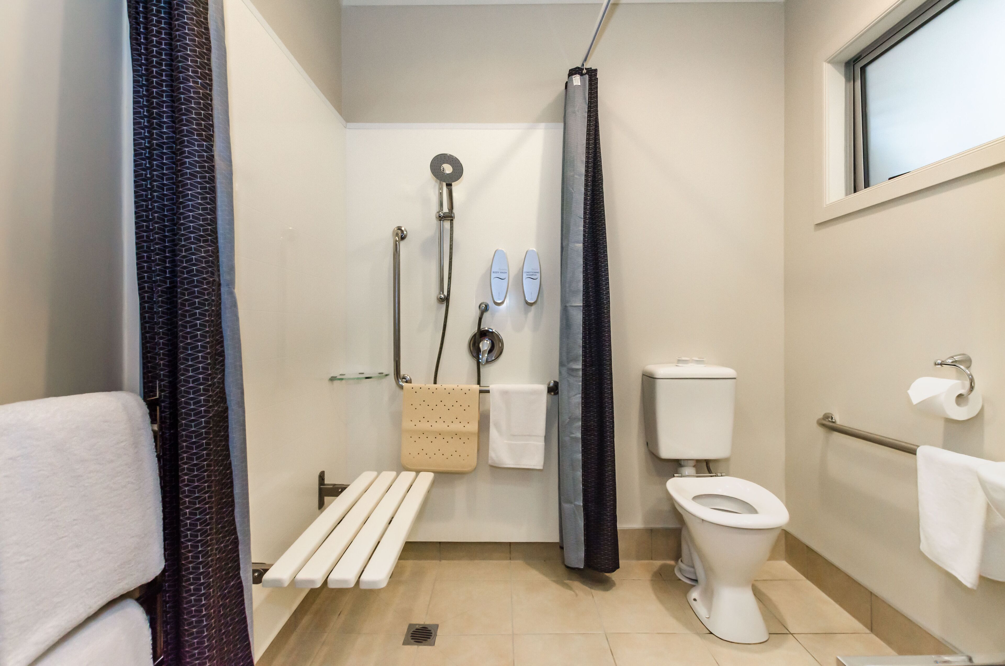 A small, modern bathroom with a shower, toilet, and a bench.