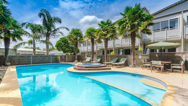 A swimming pool with lounge chairs and palm trees. - Raumati Sands Resort (Paraparaumu)