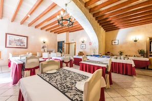 Un espace repas avec des tables dressées pour le repas, des poutres en bois au plafond et des luminaires fixés au mur.