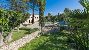 Una villa con un muro de piedra, piscina y abundante vegetación.