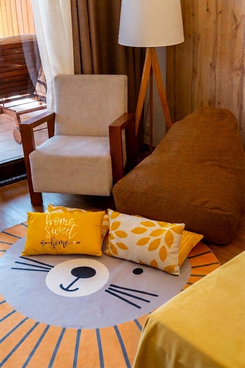 Una habitación con piso de madera, un sillón beige, un cojín marrón y una alfombra estampada con un diseño de cara de gato.
