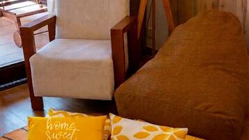 Una habitación con piso de madera, un sillón beige, un cojín marrón y una alfombra estampada con un diseño de cara de gato.