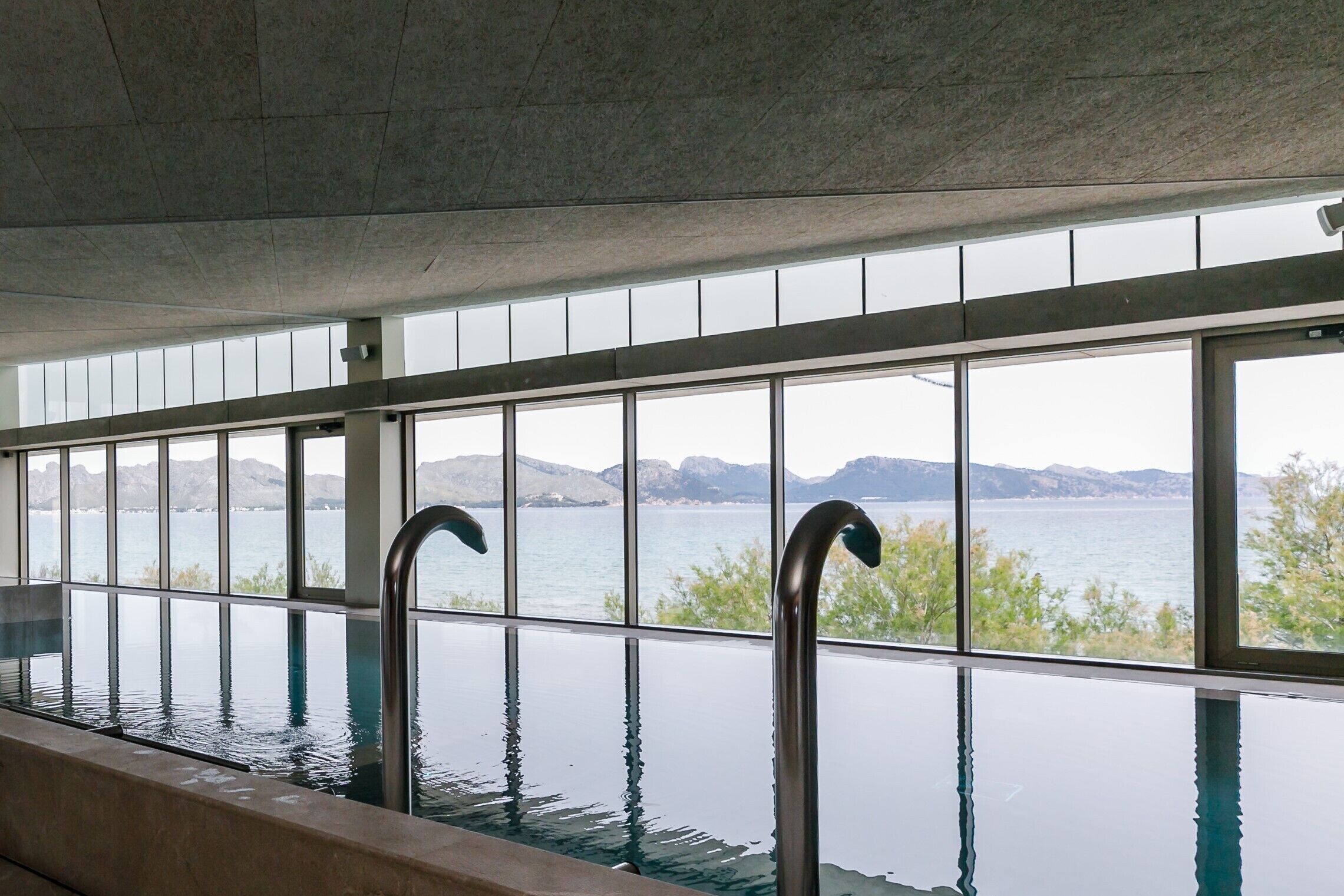 Ein Innenpool im Infinity-Design mit freiem Blick auf einen See und Berge.