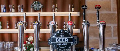 A bar with multiple beer taps, a sign reading "The Beer Experience," and shelves with bottles in the background.