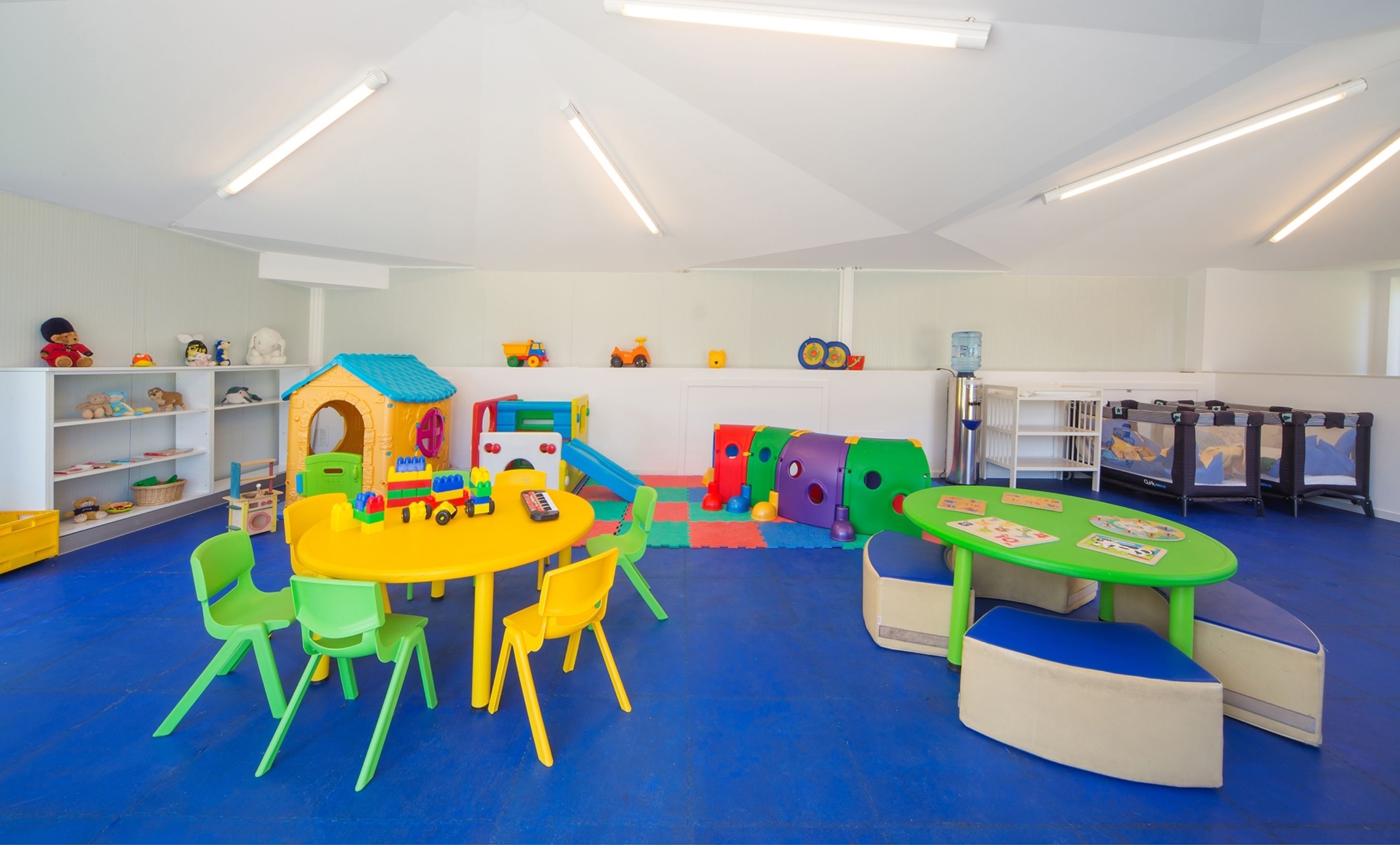 A brightly lit playroom with a blue floor, a playhouse, and various toys.