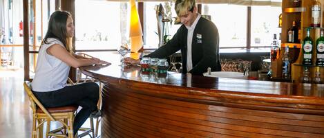 Eine Bar mit einer gebogenen Holztheke, einer Frau, die auf einem Hocker sitzt, und einem Barkeeper, der Getränke zubereitet.