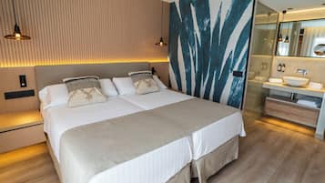 Una habitación de hotel moderna con una cama grande, cabecera de madera, lámpara de pared y baño con lavabo y espejo.