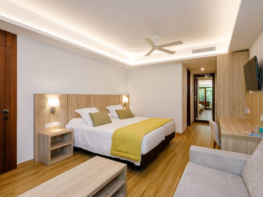 A modern hotel room with a bed, bedside tables, a desk, a chair, and a TV mounted on the wall.