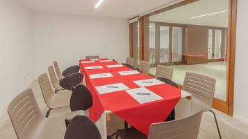 Un salón de conferencias con una larga mesa, sillas color beige y un mantel rojo.