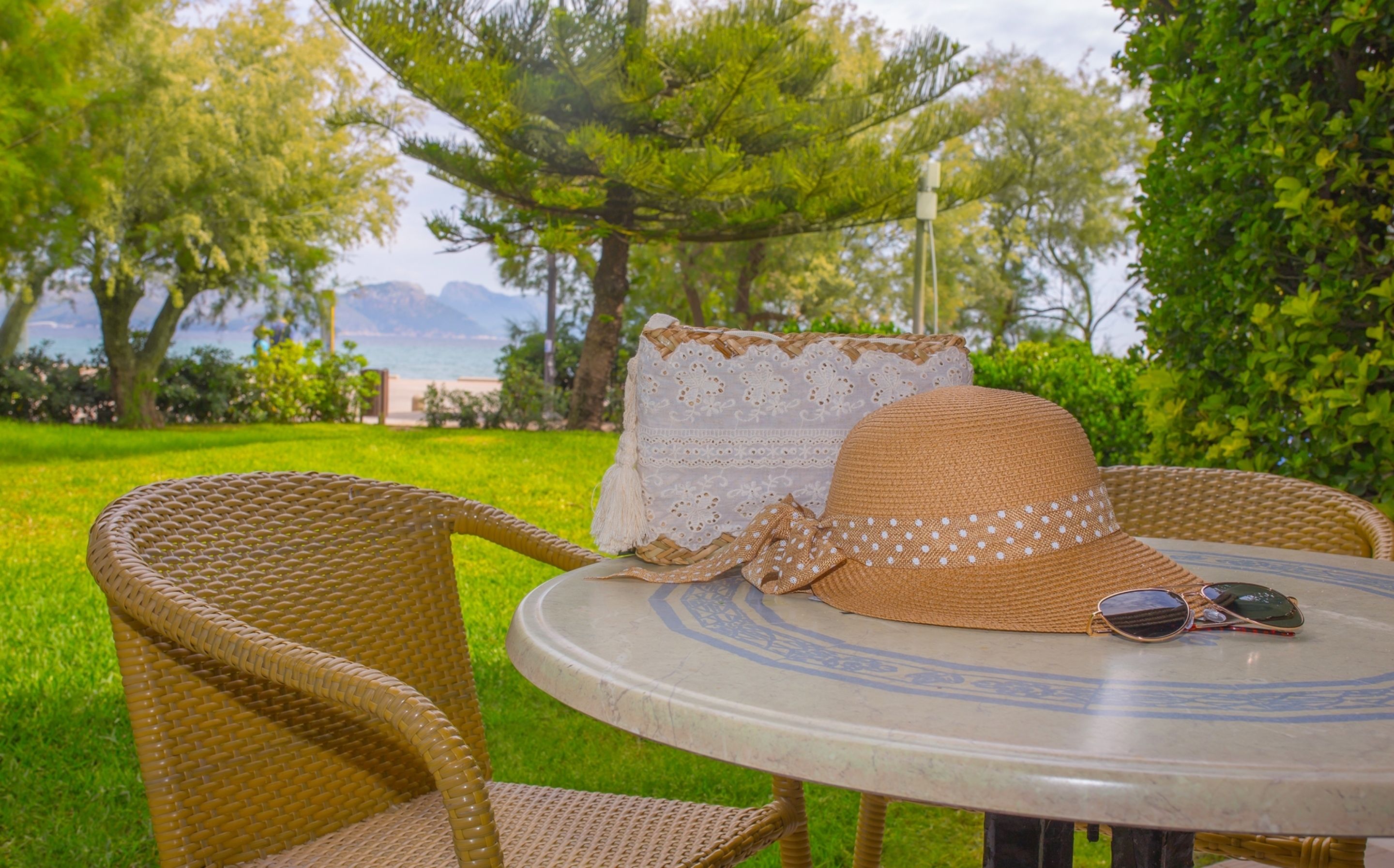 Juego de silla y mesa de mimbre al aire libre con vista a una playa y montañas al fondo.