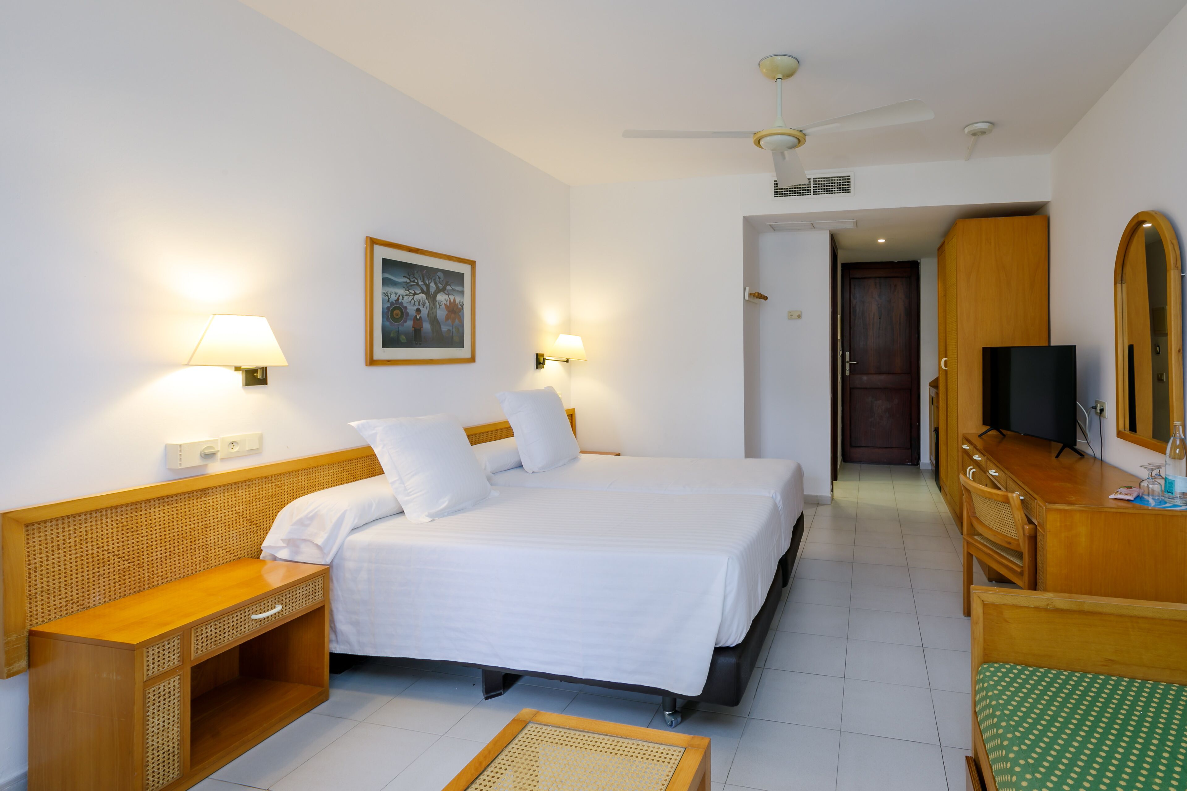 A hotel room with a bed, bedside tables, a desk, a chair, a television, and a mirror.
