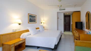 A hotel room with a bed, bedside tables, a desk, a chair, a television, and a mirror.