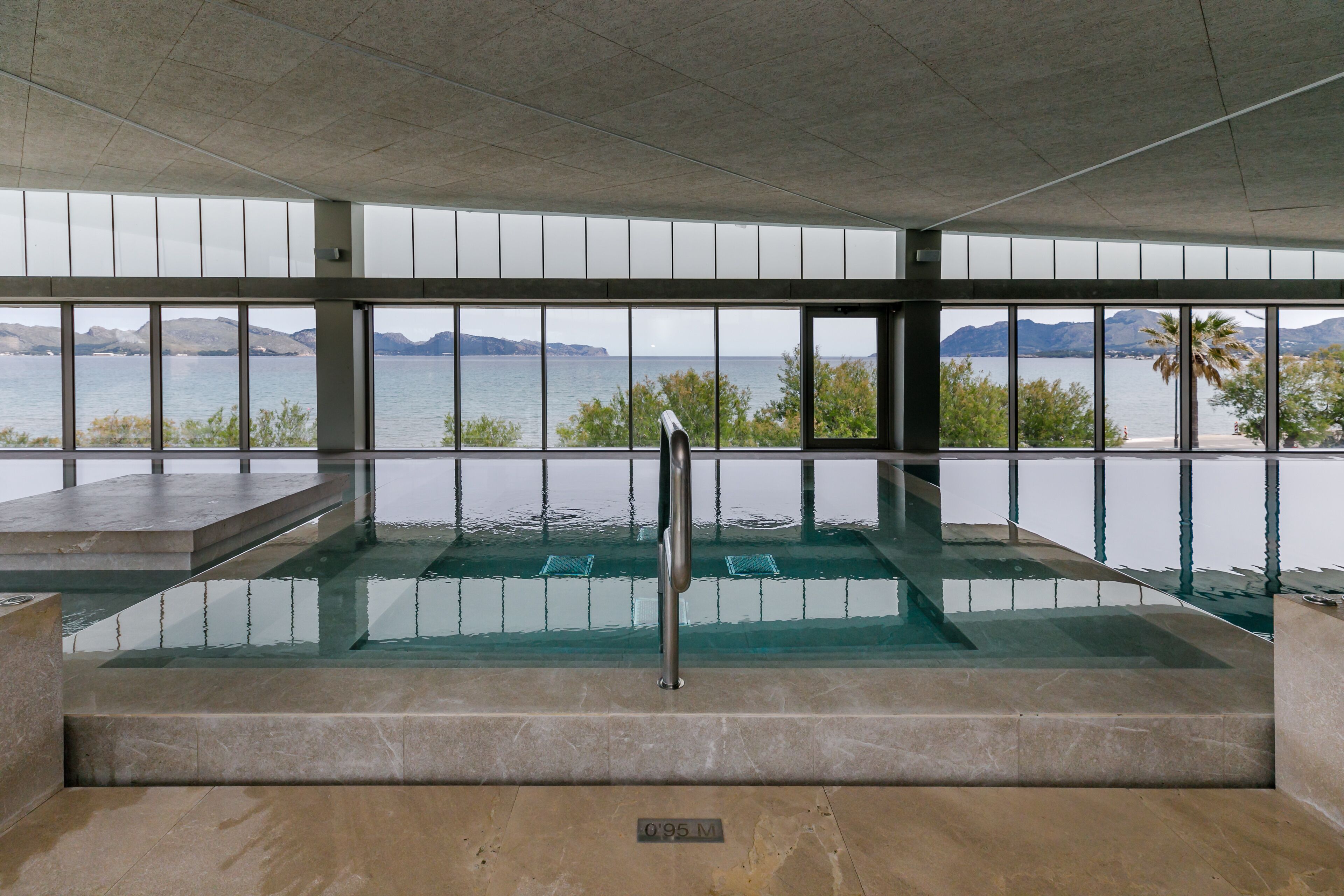 Una amplia piscina interior con vistas despejadas al mar y a las montañas a través de grandes ventanales.
