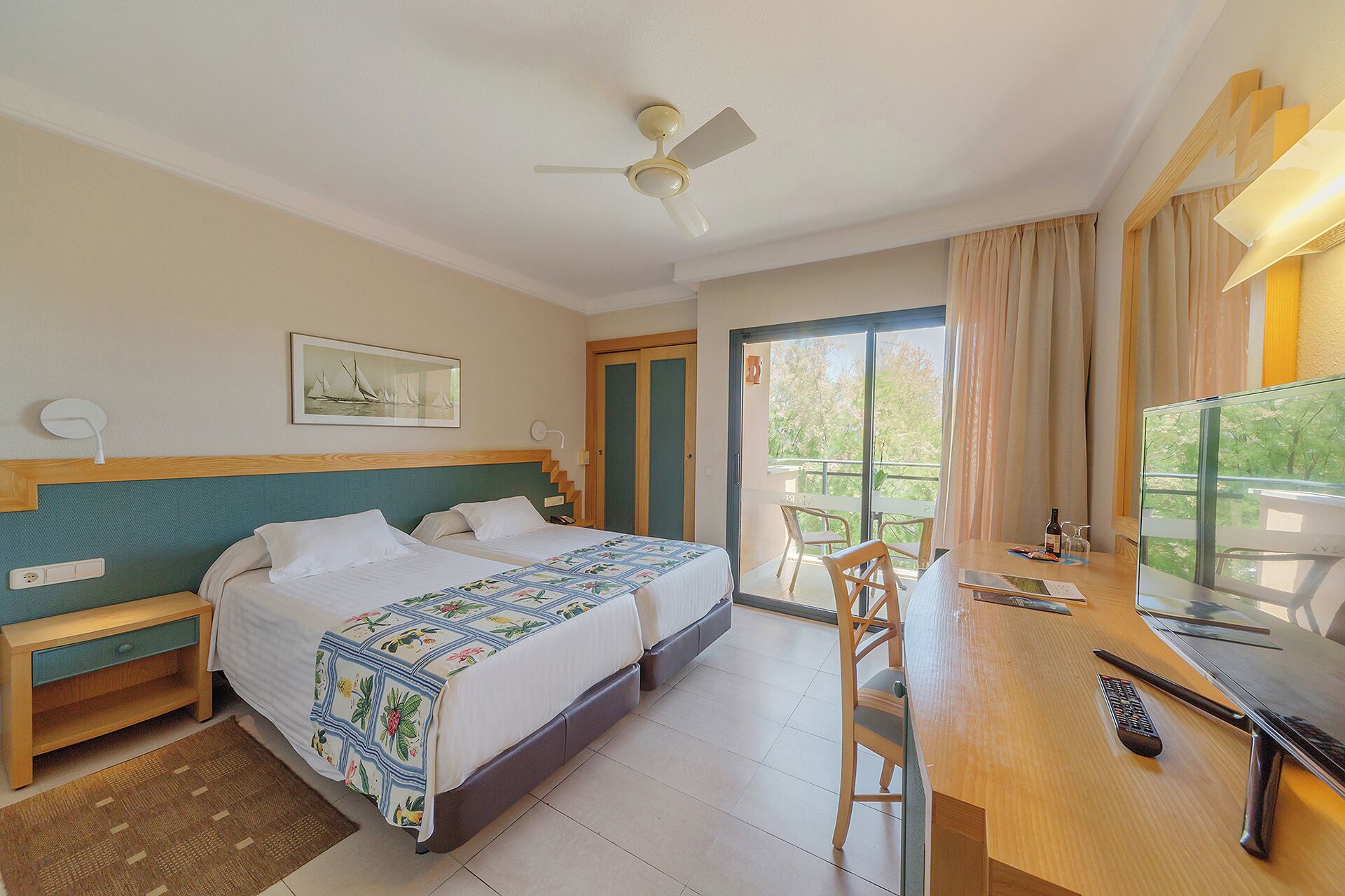 A hotel room with a bed, a desk with a chair, a television, and a balcony with curtains.