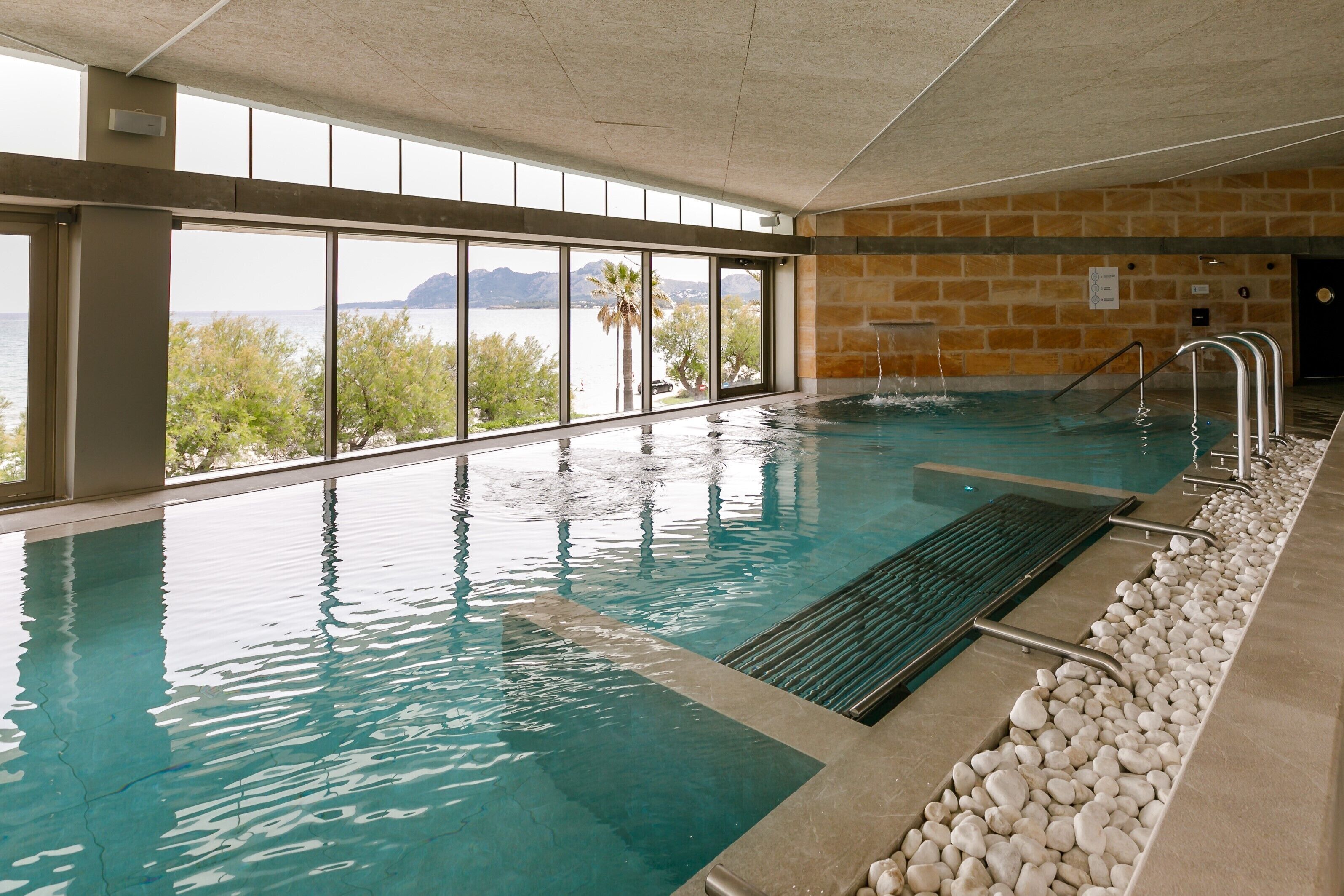 Una piscina interior con vistas despejadas a un lago y montañas a través de grandes ventanales.