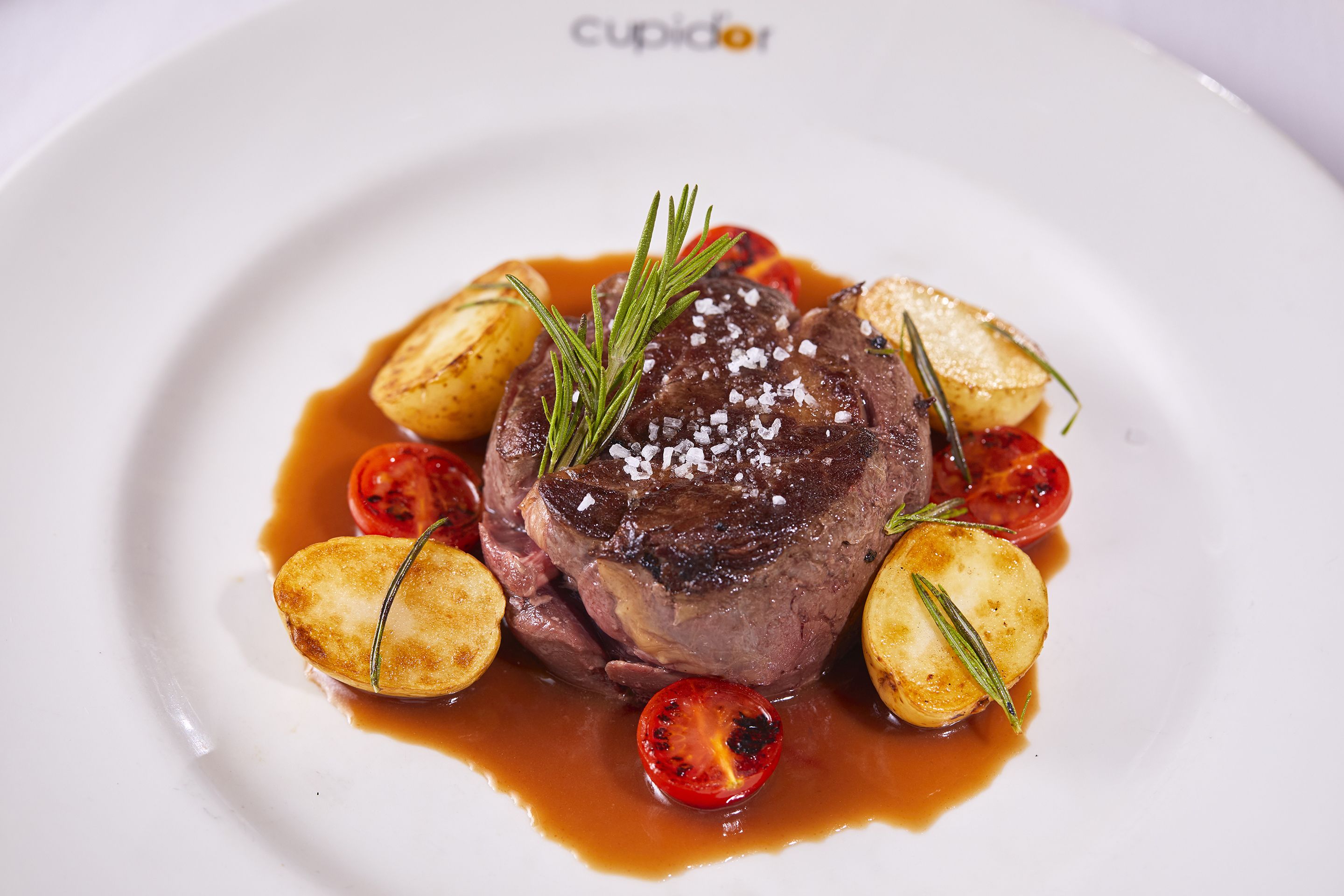Een bord met een steak, geroosterde aardappelen en gegrilde tomaten.
