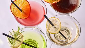 Four glasses of different colored drinks, each with a slice of fruit and a straw.