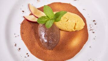 Un postre con helado de chocolate y vainilla, rodajas de manzana y hojas de menta sobre un plato blanco.