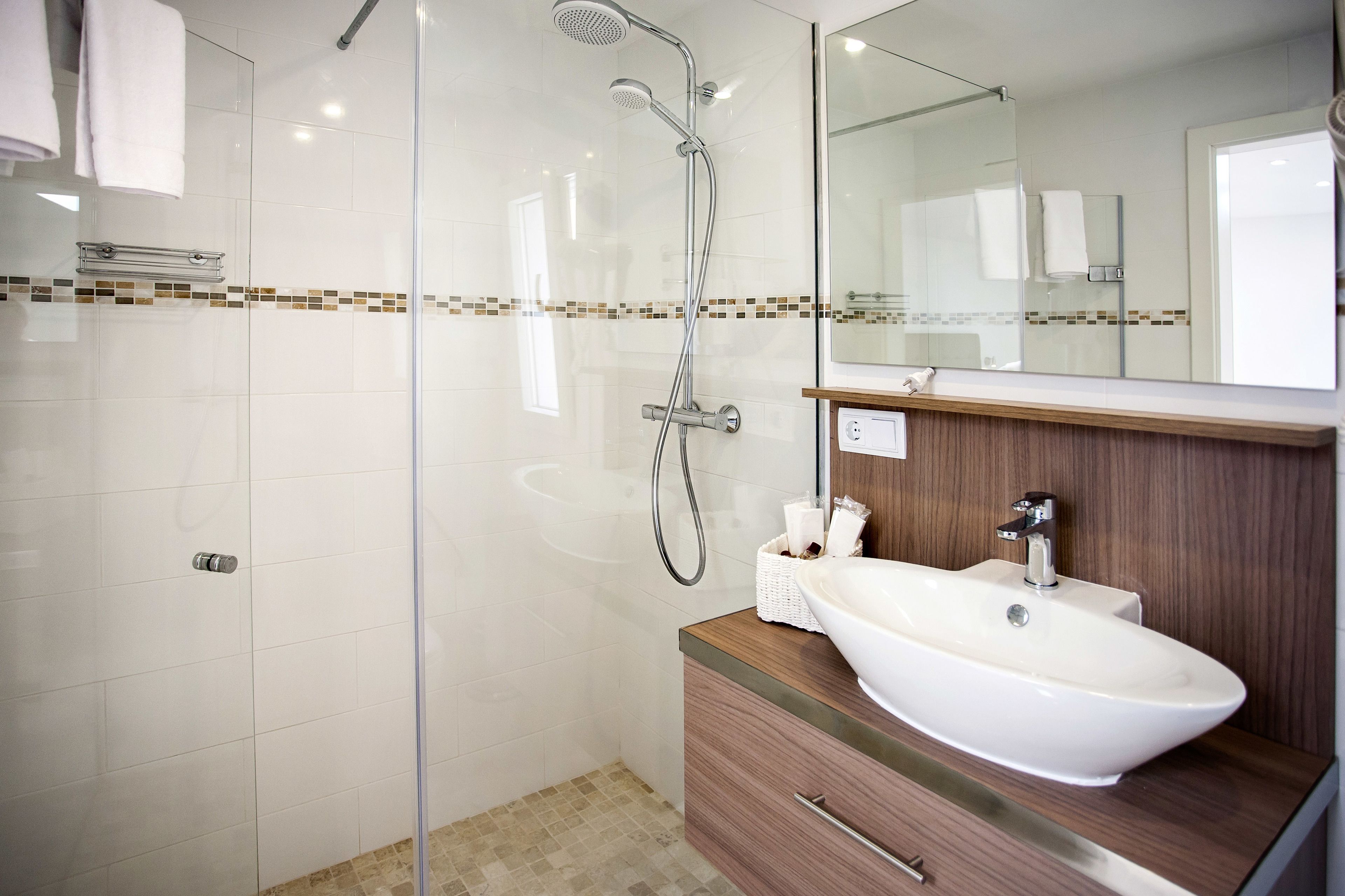 Ein modernes Badezimmer mit einer gläsernen Dusche, einem weißen Waschbecken und einem Holz-Waschtisch.
