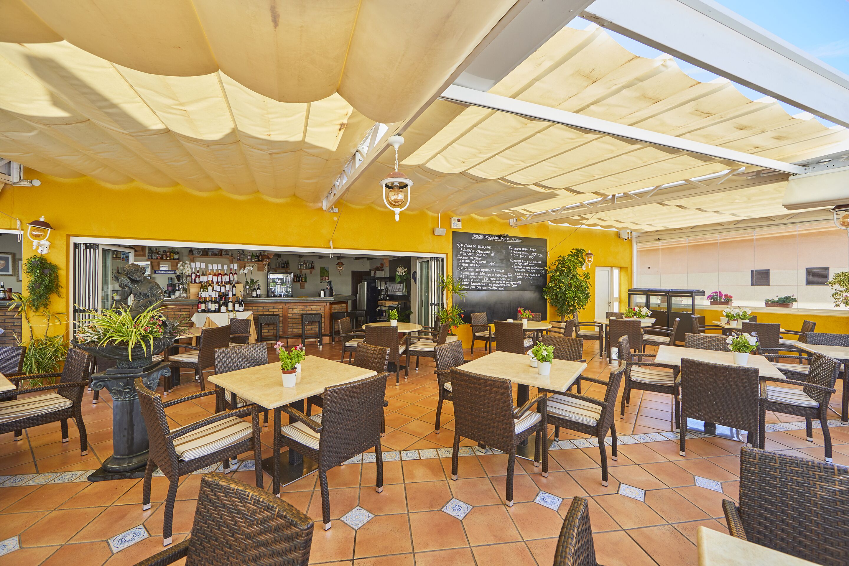 Ein Straßencafé mit Tischen, Stühlen und Pflanzen in Töpfen sowie einer Bar.