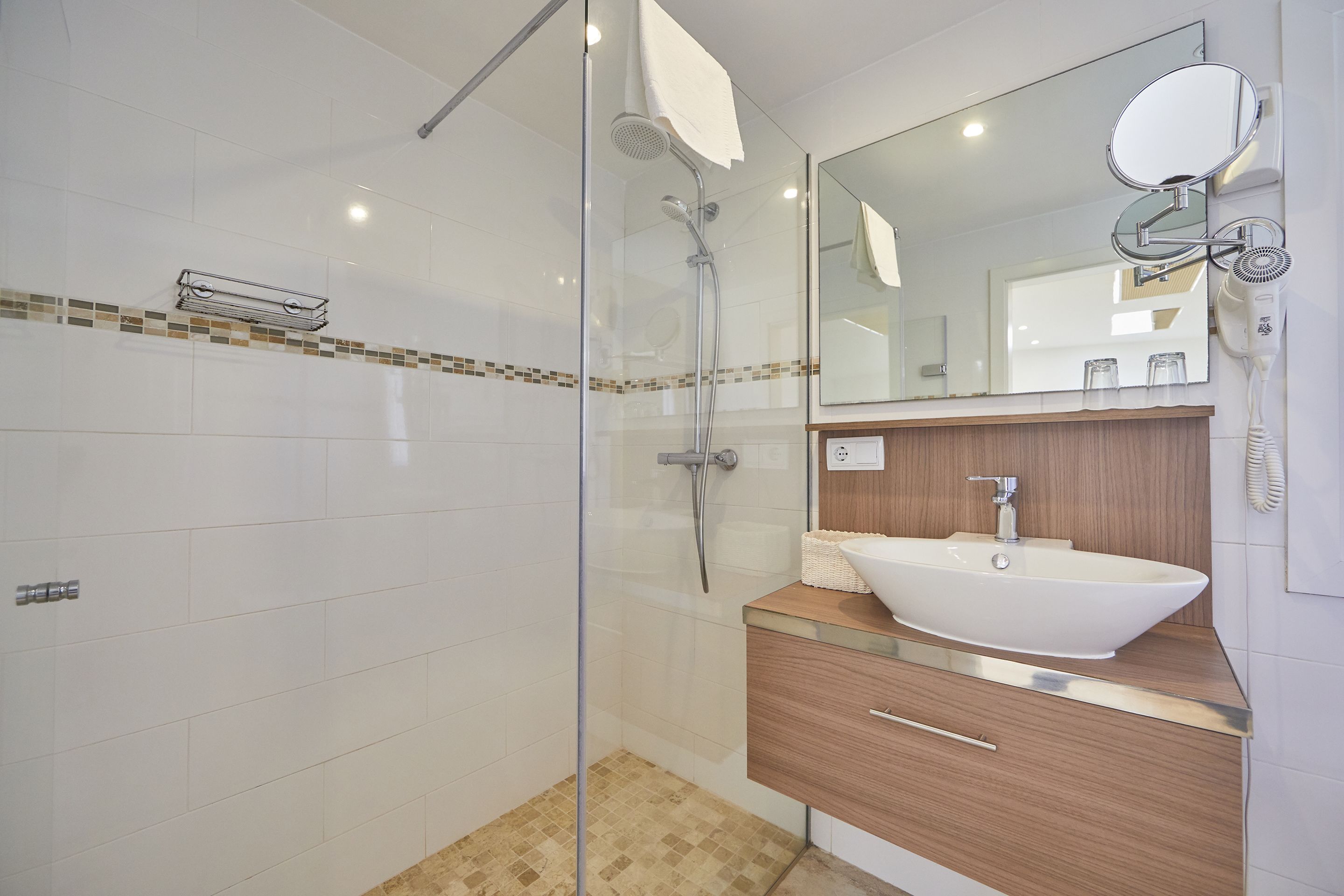 A modern bathroom with a glass shower enclosure, a wooden vanity with a white sink, and a large mirror.