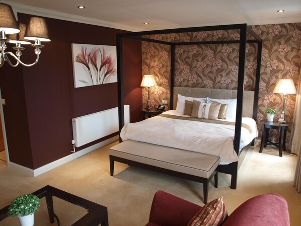 A four-poster bed with a beige bedspread, two bedside lamps, and a nightstand with a phone.